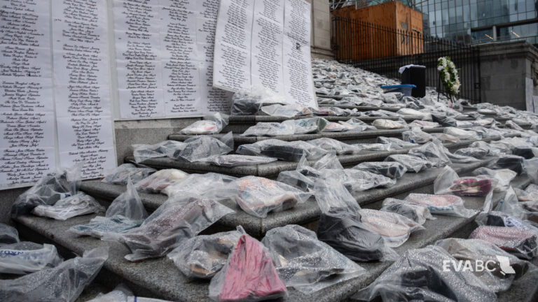 Donated shoes in plastic and a list of names of women who were killed in acts of gender-based violence at the 2023 Shoe Memorial on the Robson Street steps of the Vancouver Art Gallery.